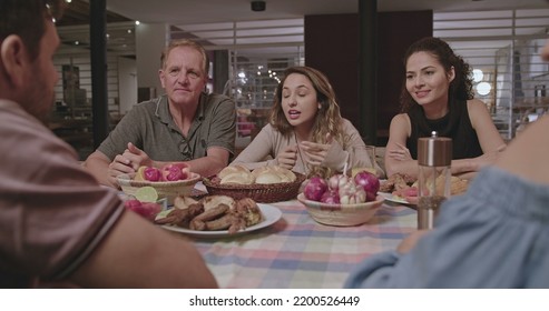 Family And Friends Gathered Outside The House At Night In Home Backyard. Group Of People Converse Sitting At Dinner Table.