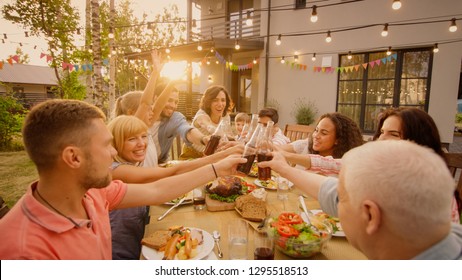 Family and Friends Gathered Together at the Table Raise Glasses and Bottles To Make a Toast and Clink Glasses. Big Family Garden Party Celebration. - Powered by Shutterstock