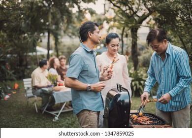 Family And Friends Gathered Together At The Table.Cooking Bbq Outdoor For A Group Of Friends.Big Family Garden Party Celebration.Diverse Neighbors Drinking Party Yard Concept.