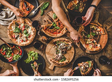 Family Or Friends Having Pizza Party Dinner. Flat-lay Of People Eating Different Kinds Of Italian Pizza, Salad And Drinking Wine Over Wooden Table, Top View. Fast Food Lunch, Gathering, Celebration