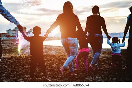 Family Friends Holding Eache Others Hands Around Fireworks At Sunset On The Beach - Adult People Having Fun With Their Children For Holidays Outdoor - Focus On Boy Silhouette - Love And Fest Concept