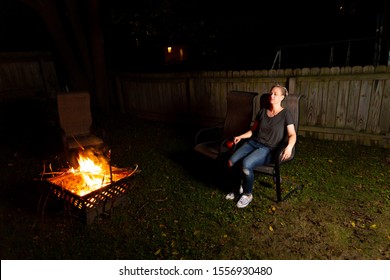 Family And Friends Sit Around A Backyard Fire Pit And Toast Smores