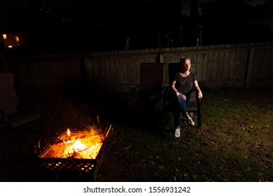 Family And Friends Sit Around A Backyard Fire Pit And Toast Smores