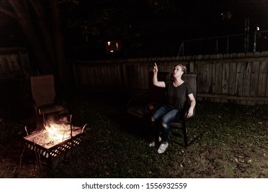 Family And Friends Sit Around A Backyard Fire Pit And Toast Smores