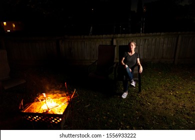 Family And Friends Sit Around A Backyard Fire Pit And Toast Smores