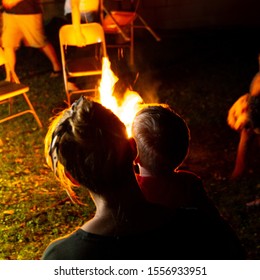 Family And Friends Sit Around A Backyard Fire Pit And Toast Smores