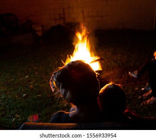 Family And Friends Sit Around A Backyard Fire Pit And Toast Smores