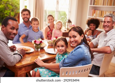 Family and friends sitting at a dining table, looking at camera