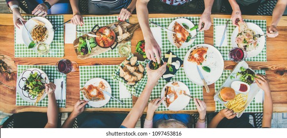 Family Or Friends Summer Party Or Outdoor Dinner. Flat-lay Of Group Of People At Big Table In Cafe Eating Verious Food Together. Summer Gathering Or Celebration Concept