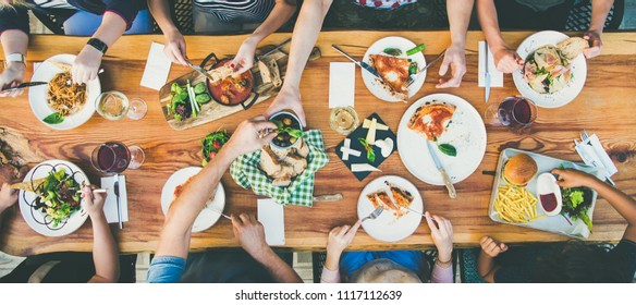 Family Or Friends Summer Party Or Outdoor Dinner. Flat-lay Of Group Of People At Big Table In Cafe Eating Verious Food Together. Summer Gathering Or Celebration Concept