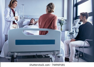 Family and friends visiting patient in hospital ward and talking with doctor. Female physician sharing the recovery of hospitalised man with his friends.