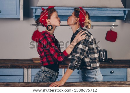 Family, friendship and people concept - happy mother with little daughter. With red lips in a bandana have fun in the home kitchen. Pin-up style photo