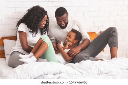 Family Fun. African american parents tickling their daughter while lying in bed together, enjoying weekend at home.