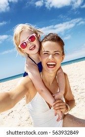 Family Fun On White Sand. Smiling Mother And Daughter In Swimsuits Taking Selfies At Sandy Beach On A Sunny Day