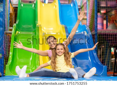 Family fun. Smiling mother and her daughter riding slide together at indoor kids playground