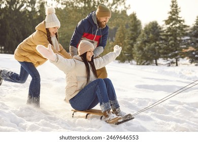 Family fun in snow. Funny parents with their teenage daughter spend time together, have fun and enjoy winter day. Woman rides sled with outstretched arms while man and teen girl push her from behind. - Powered by Shutterstock