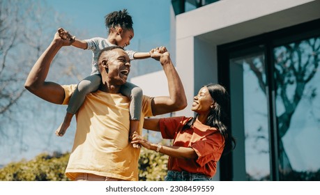 Family fun time with mom and dad at home. Couple playing with their daughter and creating happy childhood memories. Dad carrying his daughter on his shoulders and standing next to mom.