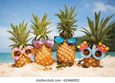 Family of funny attractive pineapples in stylish sunglasses on the sand against turquoise sea. Tropical summer vacation concept. Happy sunny day on the beach of tropical island. Family holiday - Shutterstock ID 633460052