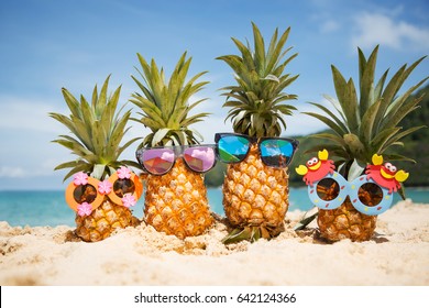 Family of funny attractive pineapples in stylish sunglasses on the sand against turquoise sea. Tropical summer vacation concept. Happy sunny day on the beach of tropical island. Family holiday - Shutterstock ID 642124366