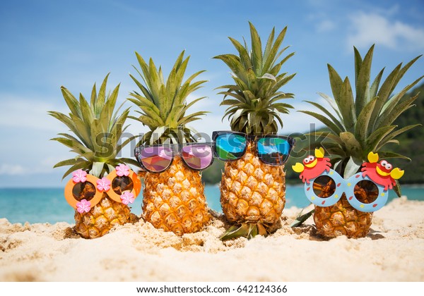 青緑色の海に面した砂の上に スタイリッシュなサングラスをかけた おかしな魅力的なパイナップルのファミリー 熱帯の夏休みのコンセプト 熱帯島の海岸での幸せな晴れの日 家族の休日 の写真素材 今すぐ編集