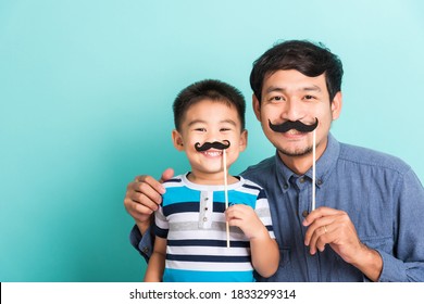 Family funny happy hipster father and his son kid holding black mustache props for the photo booth close face, studio shot isolated on a blue background, November men health awareness - Powered by Shutterstock