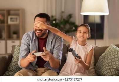 Family, Gaming And Entertainment Concept - Happy Father And Little Daughter With Gamepads Playing Video Game At Home