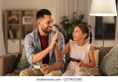 Family, Gaming And Entertainment Concept - Happy Father And Little Daughter With Gamepads Playing Video Game At Home