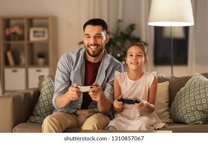 Family, Gaming And Entertainment Concept - Happy Father And Little Daughter With Gamepads Playing Video Game At Home