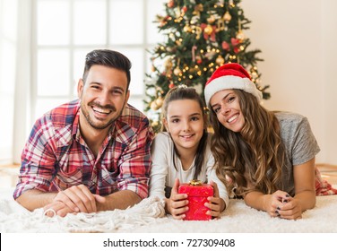 Family gather around a Christmas tree, holding a  present
