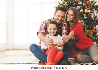 Family Gathered Around A Christmas Tree, Using A Tablet 