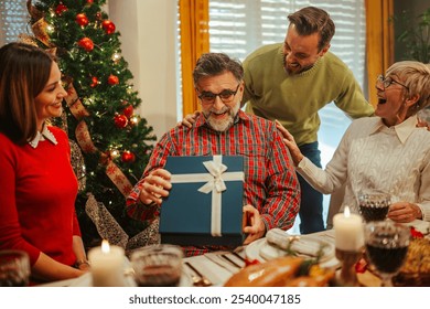 Family is gathered around a festive table enjoying their christmas dinner and giving a present to their father and grandfather - Powered by Shutterstock