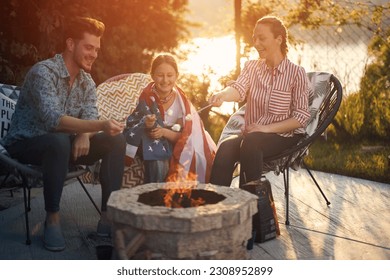 A family gathers around a crackling fire, joyfully roasting marshmallows as they celebrate Independence Day. Little girl wrapped in the embrace of an American flag, her eyes sparkling with excitement. - Powered by Shutterstock