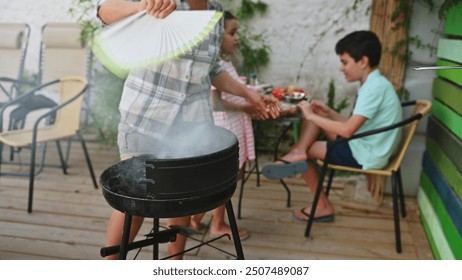 A family gathers for a summer seafood barbecue. A parent fans smoke from the grill, while children relax on the patio. Perfect for family, summer, and outdoor dining themes. - Powered by Shutterstock