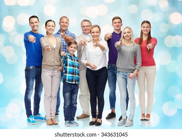 family, gender, generation and gesture concept - group of happy people pointing finger on you over blue holidays lights background