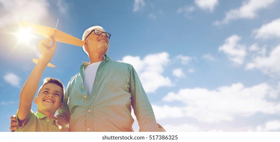 Family, Generation, Future, Dream And People Concept - Happy Grandfather And Grandson With Toy Airplane Over Blue Sky And Clouds Background