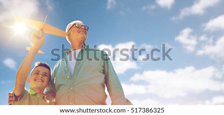family, generation, future, dream and people concept - happy grandfather and grandson with toy airplane over blue sky and clouds background