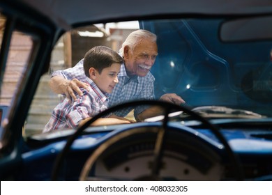 Family And Generation Gap. Old Grandpa Spending Time With His Grandson. The Senior Man Shows The Engine Of A Vintage Car From The 60s To The Preteen Child. They Smile Happy. 