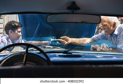 Family And Generation Gap. Old Grandpa Spending Time With His Grandson. The Senior Man Asks The Preteen Child To Help Him Fixing The Engine Of A Vintage Car From The 60s. They Smile Happy. 