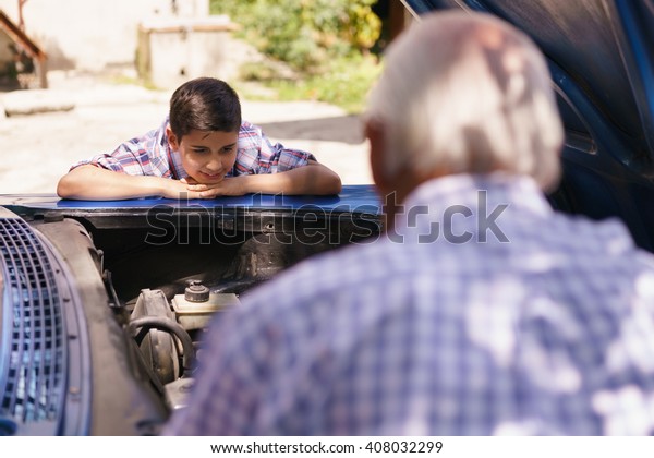 Family and\
Generation gap. Old grandpa spending time with his grandson. The\
senior man shows the engine of a vintage car from the 60s to the\
preteen child. They boy smiles\
happy.
