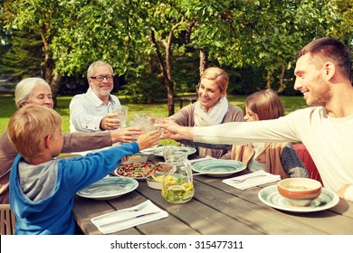 Family, Generation, Home, Holidays And People Concept - Happy Family Having Dinner And Clinking Glasses In Summer Garden