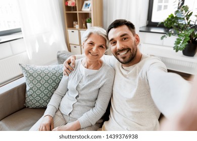 family, generation and people concept - happy smiling senior mother with adult son taking selfie at home