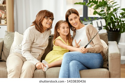 family, generation and technology concept - happy mother, daughter and grandmother taking picture by smartphone on selfie stick at home - Shutterstock ID 1433830436