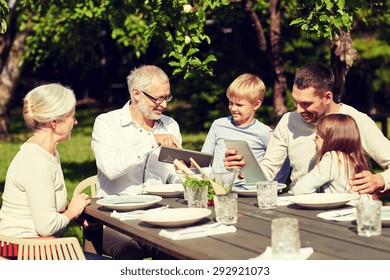 Family, Generation, Technology, Home And People Concept - Happy Family With Tablet Pc Computers Sitting At Table In Summer Garden