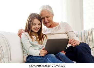 family, generation, technology and people concept - smiling granddaughter and grandmother with tablet pc computer sitting on couch at home - Powered by Shutterstock