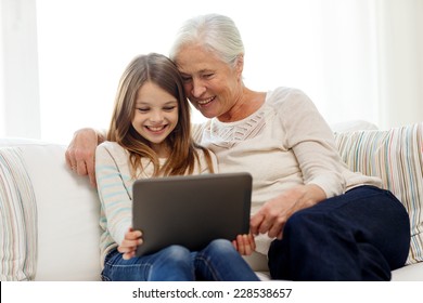 family, generation, technology and people concept - smiling granddaughter and grandmother with tablet pc computer sitting on couch at home - Powered by Shutterstock