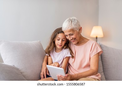 Family, generation, technology - smiling granddaughter and grandmother with tablet pc computer sitting on couch at home. Cheerful Girl sitting at home with her grandmother using tablet computer - Powered by Shutterstock