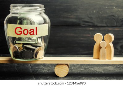 Family And Glass Jar With The Inscription Goal. The Concept Of Achieving Family Goals. The Accumulation Of Money For The Execution Of Targets. Achievement And Motivation. Family Budget Planning