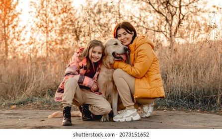 Family With Golden Retriever Dog With Sunset Light Outdoors. Mother Girl And Daughter Child With Doggy Pet Labrador At Nature At Autumn