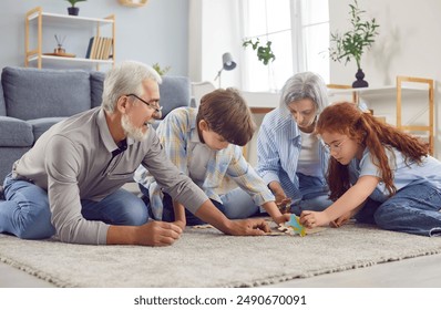 Family of grandmother, grandfather and grandchildren playing on the floor in a puzzle in the living room at home. Smiling senior couple collecting jigsaw with kids. Family leisure and people concept. - Powered by Shutterstock