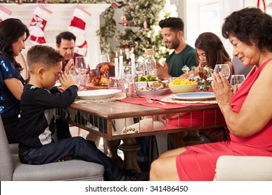 Family With Grandparents Saying Grace Before Christmas Meal